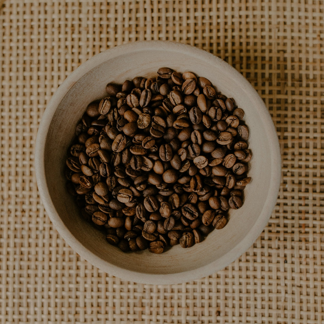 Roasted coffee beans fill a small, rustic bowl.