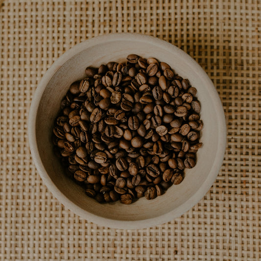 Roasted coffee beans fill a small, rustic bowl.